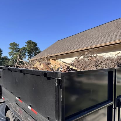Dumpster trailer loaded with branches beside a house