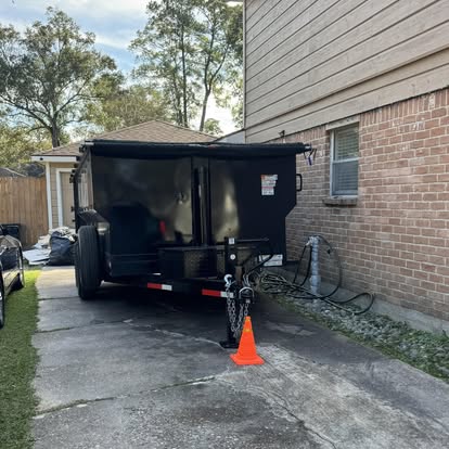Dumpster trailer parked beside a home with a safety cone at the hitch