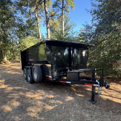 Empty black dumpster trailer parked under tall trees
