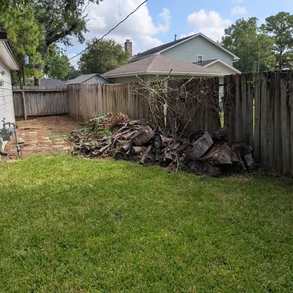 Backyard brush and wood debris stacked near a fence before pickup